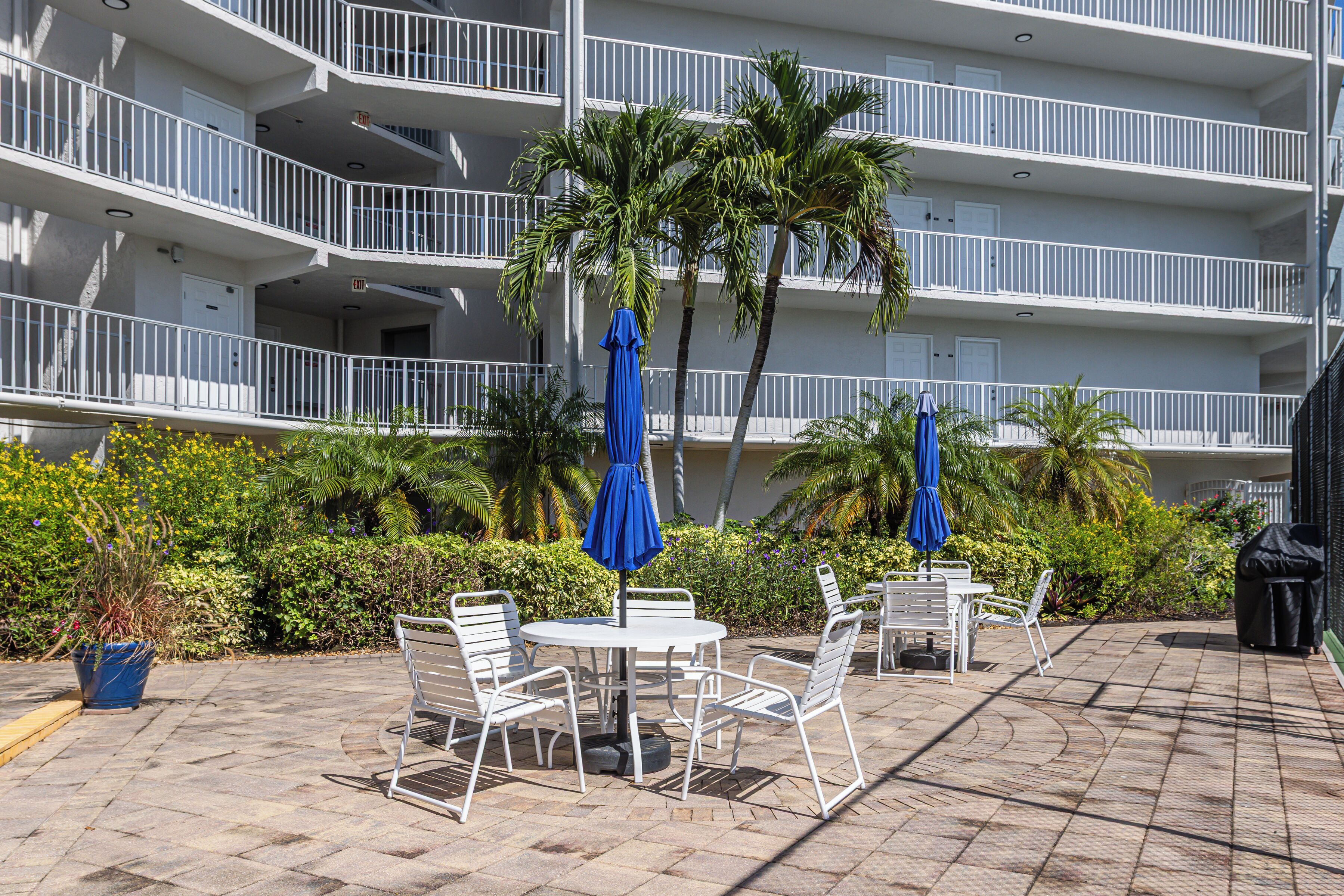 A multi-story building with balconies, outdoor seating with umbrellas, and a variety of plants.