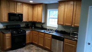 A kitchen with wooden cabinets, a black stove, a dishwasher, and a window. - SPACIOUS Cartersville HOME that SLEEPS UP TO 13 PEOPLE and 12 min. to Lakepoint! (Cartersville)