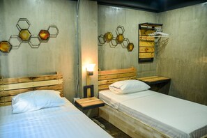 Una habitación con dos camas, cabeceros de madera, un estante montado en la pared y decoración hexagonal.