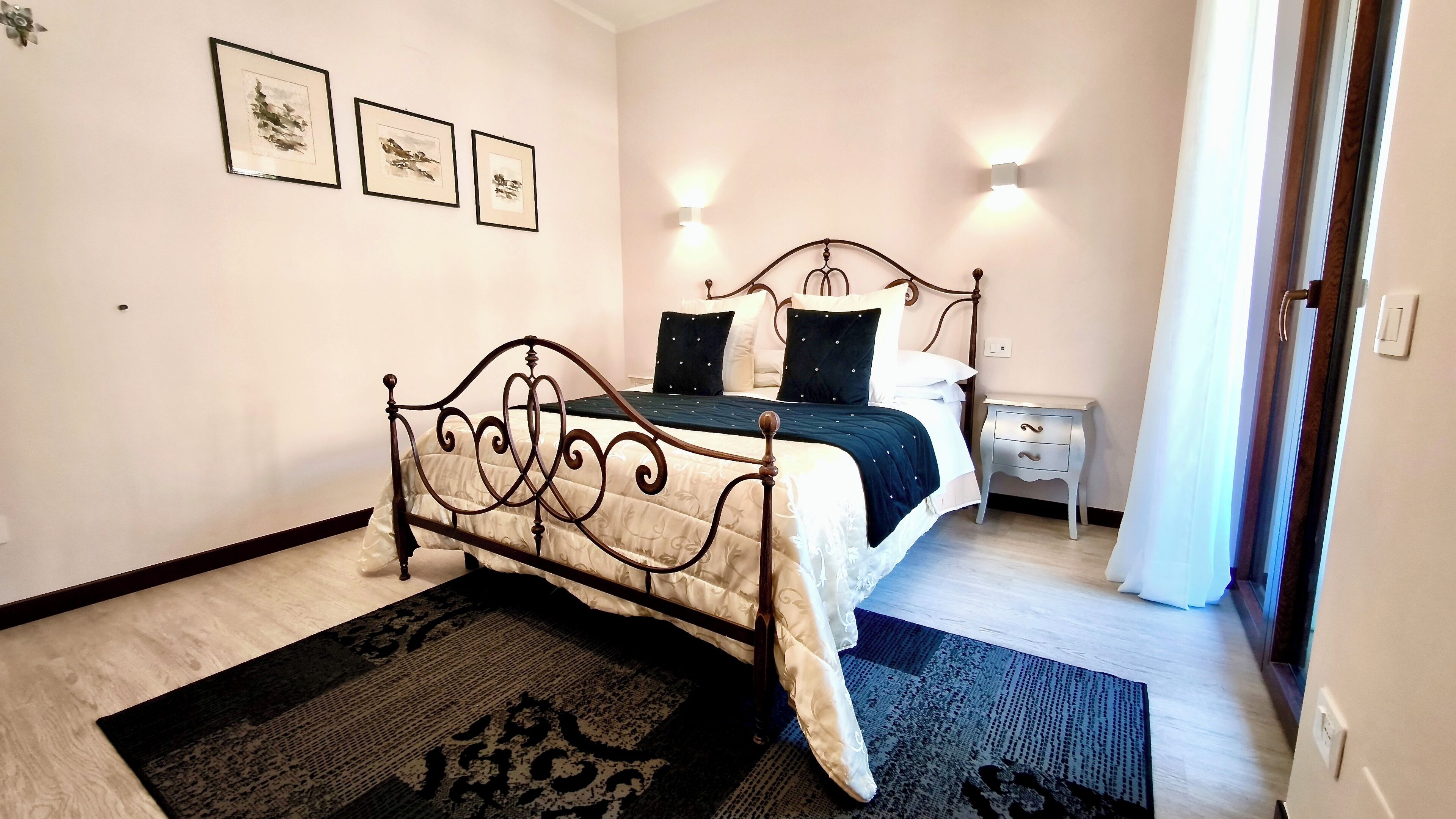 Une chambre à coucher comprenant un lit, une table de chevet, une lampe fixée au mur et trois tableaux encadrés.