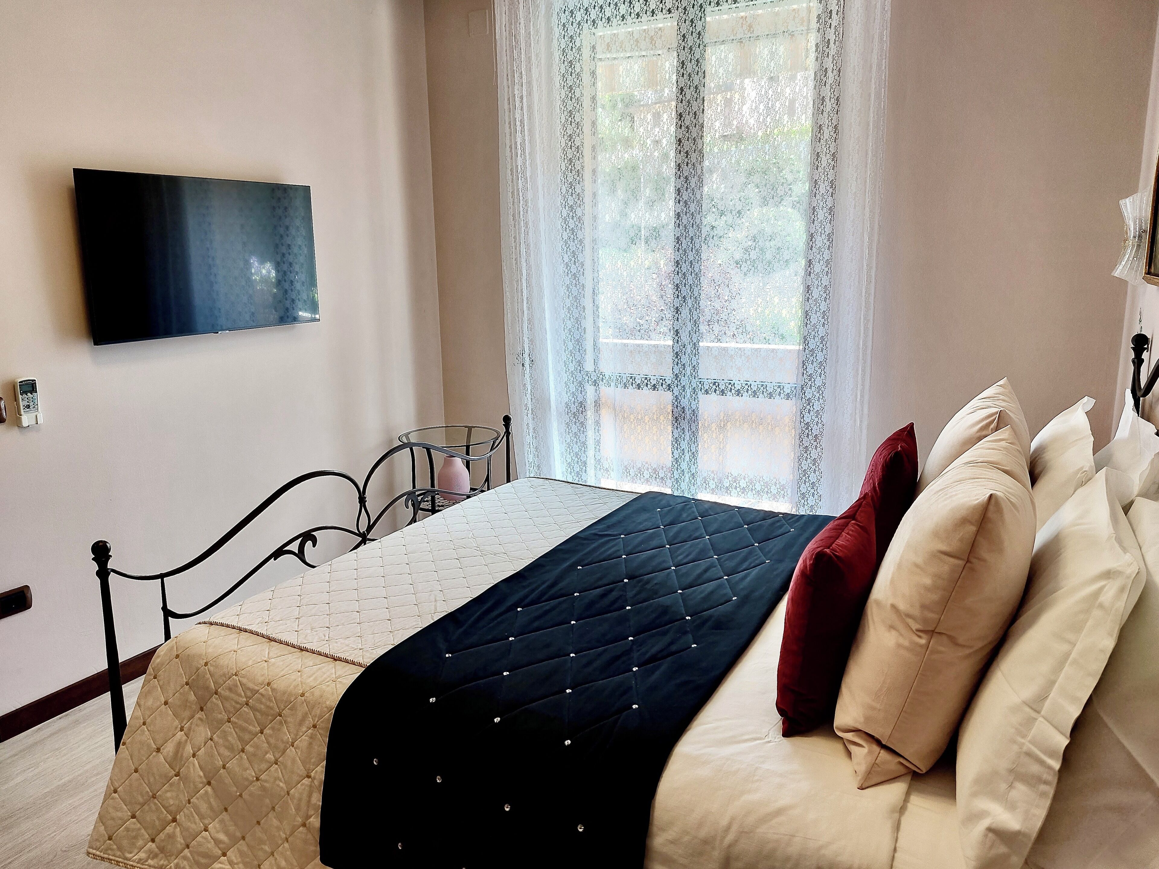 Ein Schlafzimmer mit einem Bett, einem an der Wand befestigten Fernseher und einem Fenster mit Spitzenvorhängen.