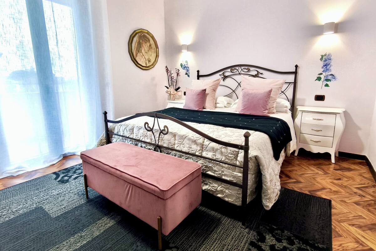 Un dormitorio con cama, mesita de noche, reloj de pared y ventana con cortinas.