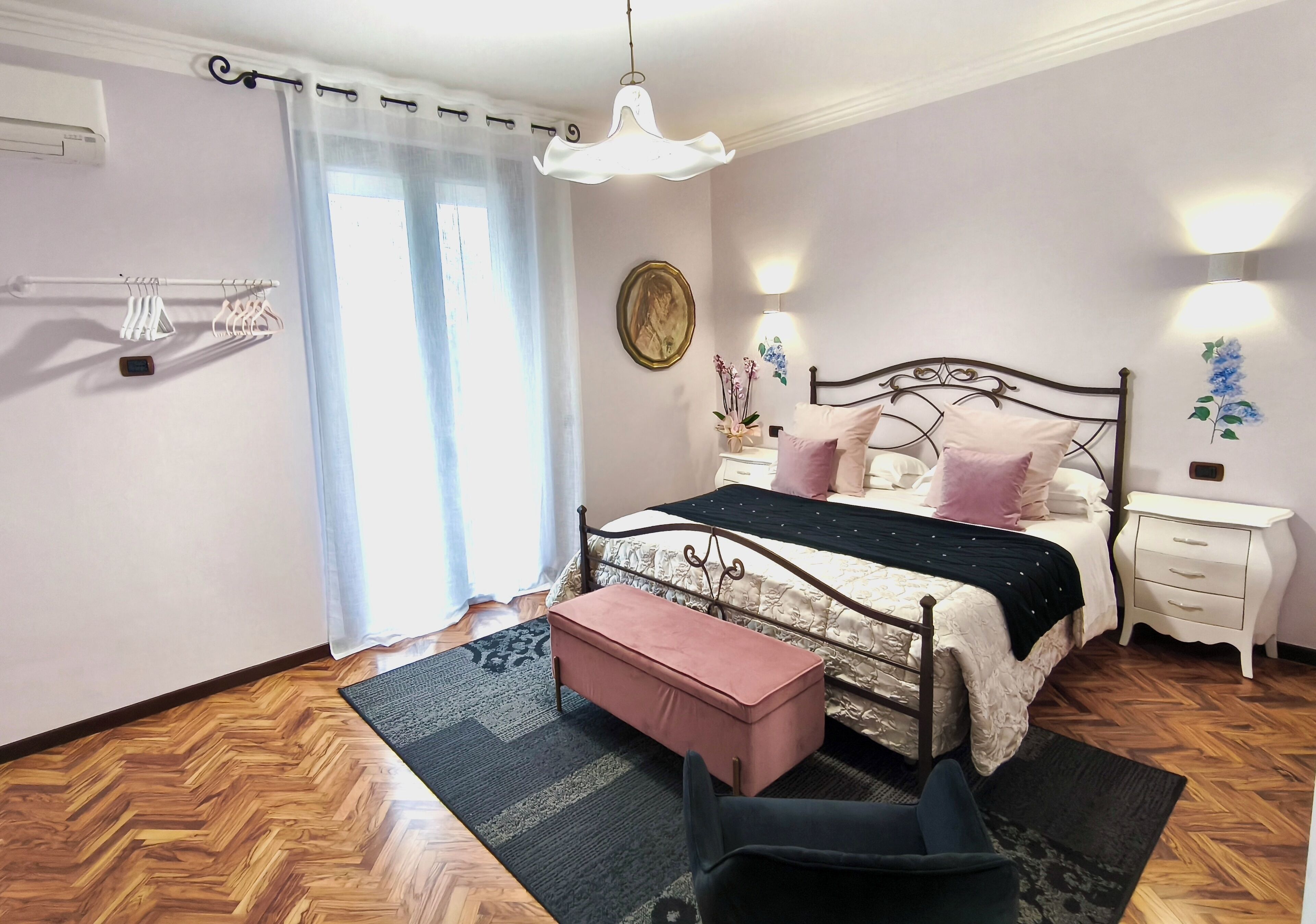 Un dormitorio con cama, mesita de noche, banqueta y lámpara colgante.