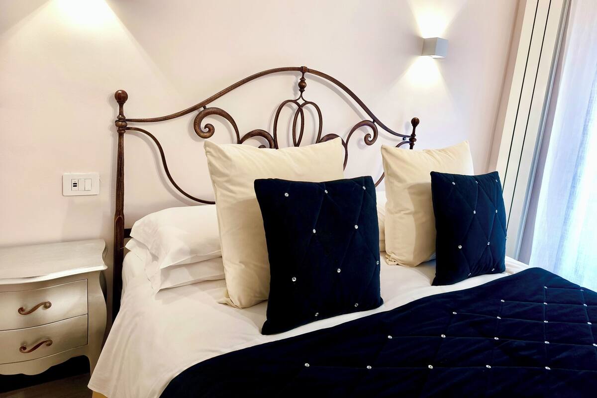 Una cama bien hecha con almohadas blancas y azul oscuro, un edredón azul oscuro y un cabecero de metal.