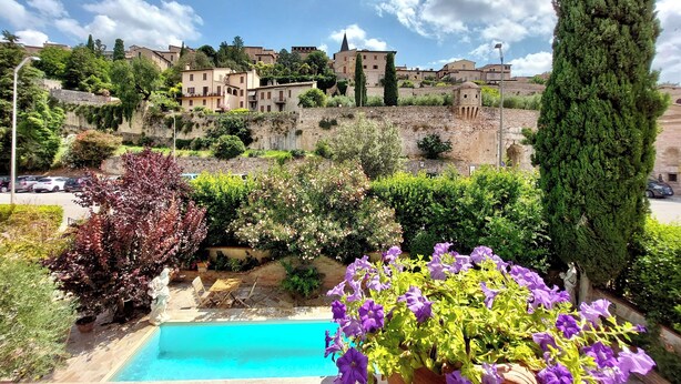 Una piscina rodeada de exuberante vegetación y flores púrpuras, con edificios al fondo.