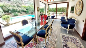 Un amplio comedor con mesa de vidrio y sillas tapizadas en azul, con vistas a una piscina y un jardín exuberante.
