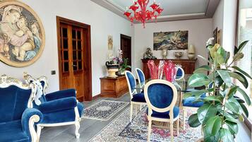 A room with a dining area, a large painting, a chandelier, and a potted plant.