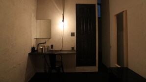Une petite pièce peu éclairée, avec un bureau, une chaise et un climatiseur fixé au mur.