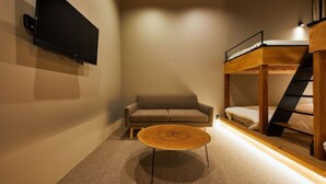 Une pièce comprenant un lit superposé, un canapé, une table basse et un téléviseur à écran plat fixé au mur.