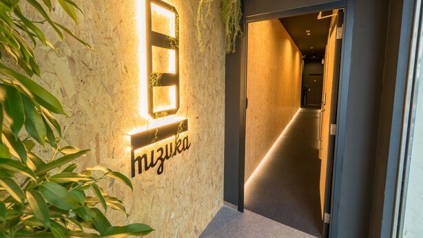 Un couloir avec un mur en bois, une enseigne indiquant « Mizuoka », et une plante suspendue au plafond.