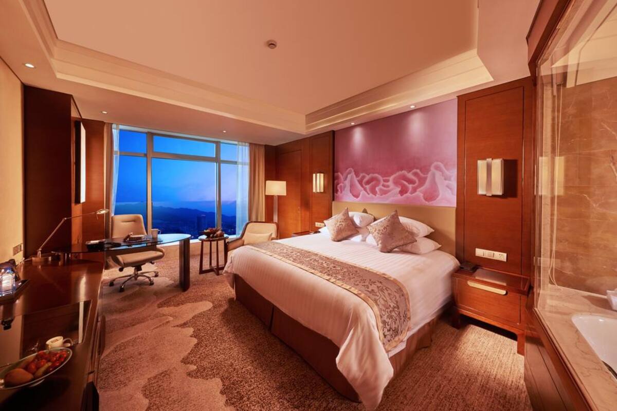 Ein Hotelzimmer mit einem großen Bett, einem Schreibtisch, einem Stuhl und Blick auf die Stadtlandschaft.