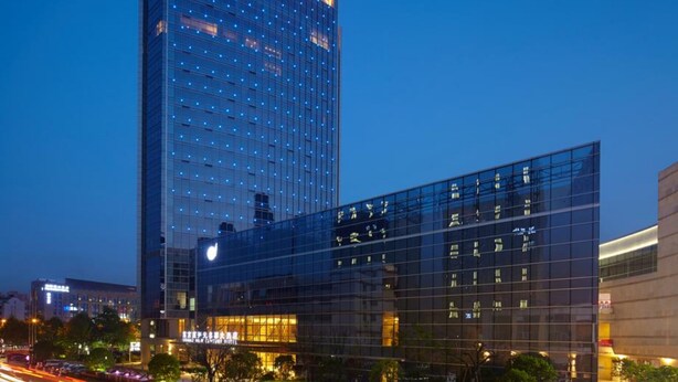 Ein modernes Hotel mit Glasfassade, ein markantes Gebäude im Hintergrund und eine belebte Straße mit Lichtspuren.