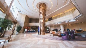 Eine großzügige Lobby mit einer zentralen Säule, Sitzbereichen und einer Rezeption.