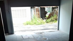 Un garaje con piso de concreto, una puerta de metal y vista a un área verde exterior.