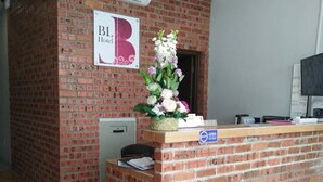 Una recepción con pared de ladrillo, un equipo de aire acondicionado, un letrero con la letra 'B' y un arreglo floral.