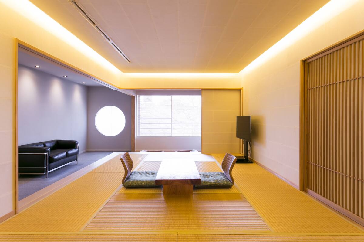 A traditional Japanese-style room with tatami flooring, a low table, cushions, and a black sofa.