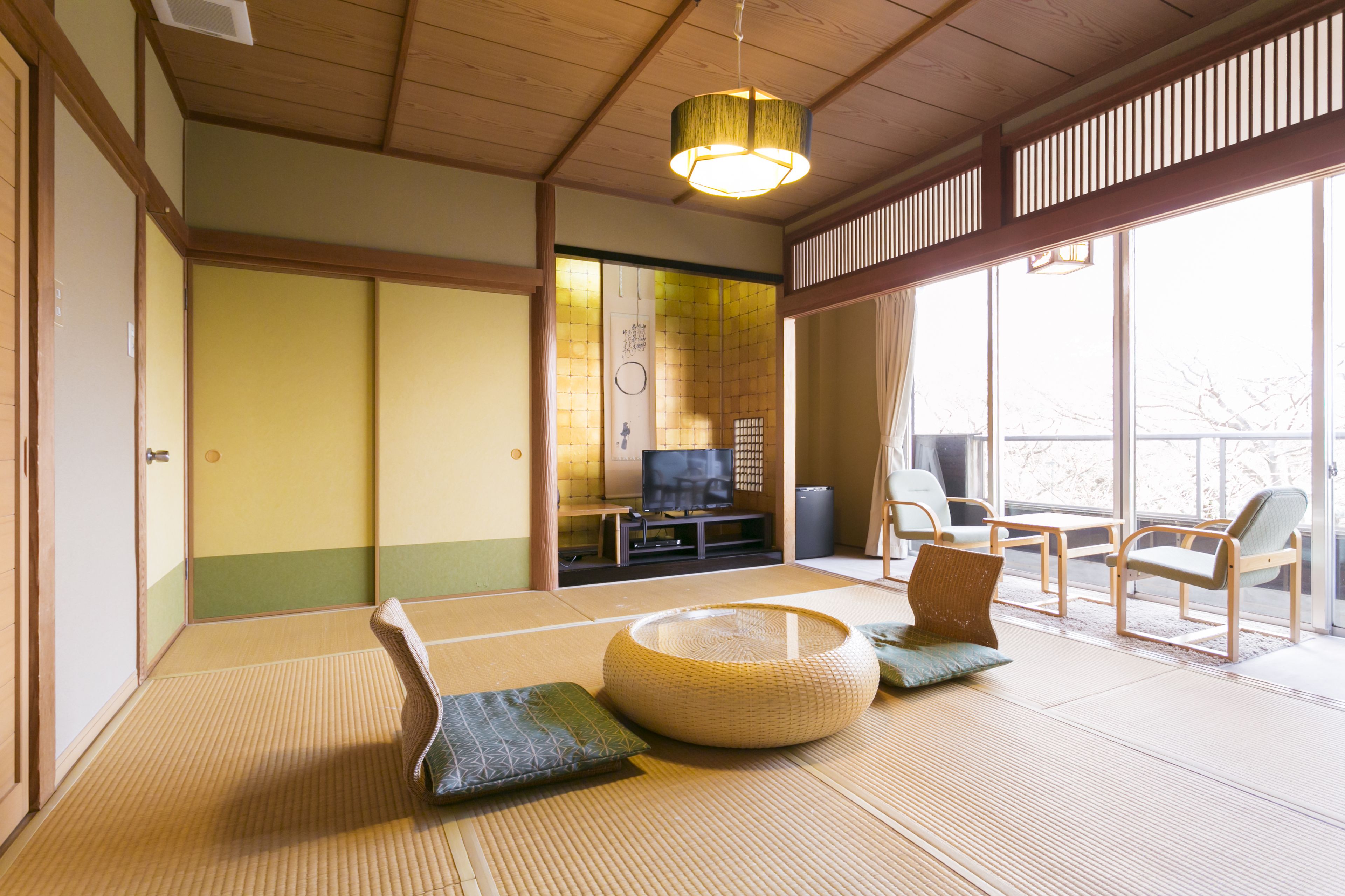 A traditional Japanese room with tatami flooring, a low table, cushions, and a television set.