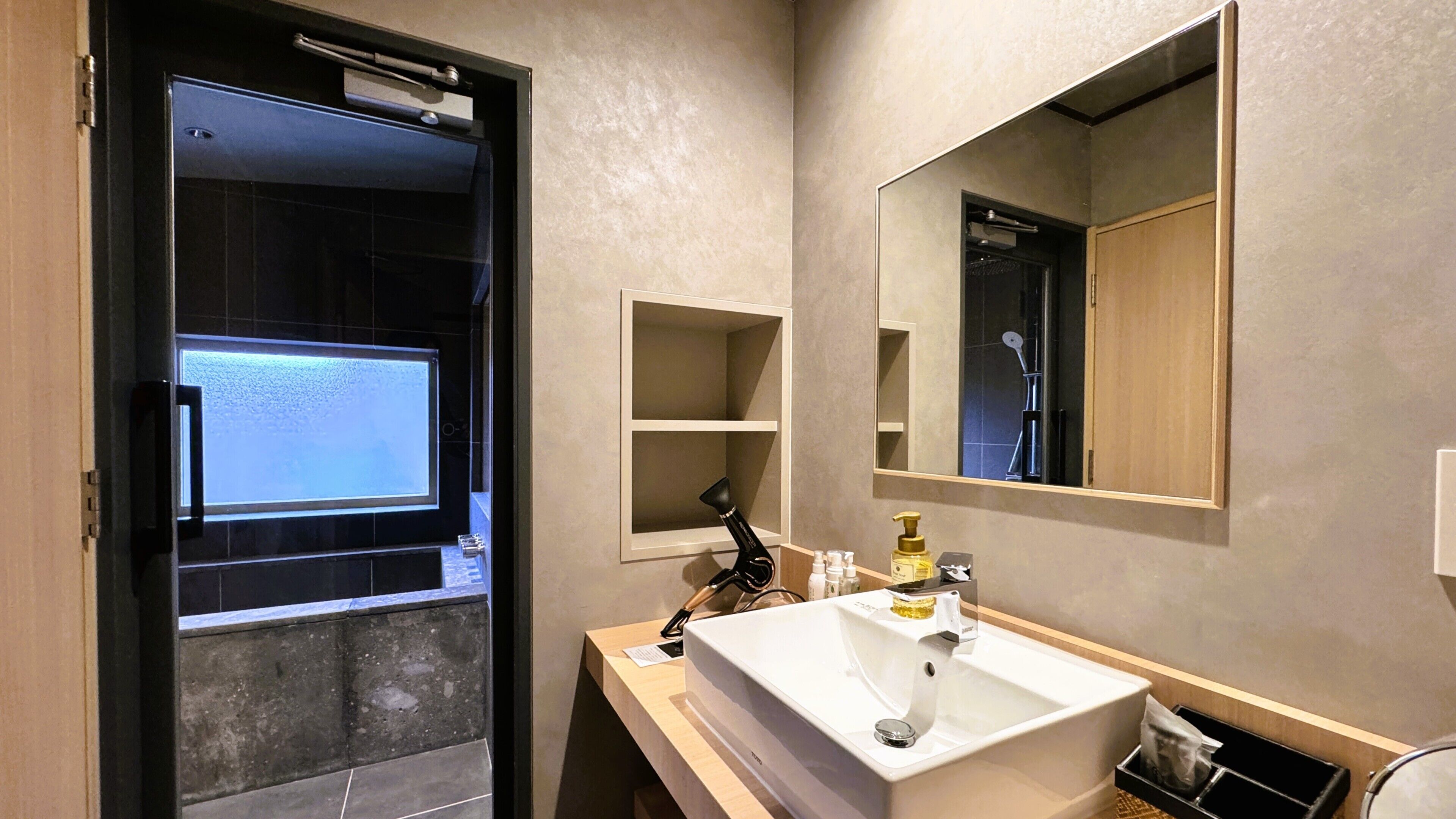 A bathroom with a large mirror, a sink, a shower, and a door leading to a shower area.