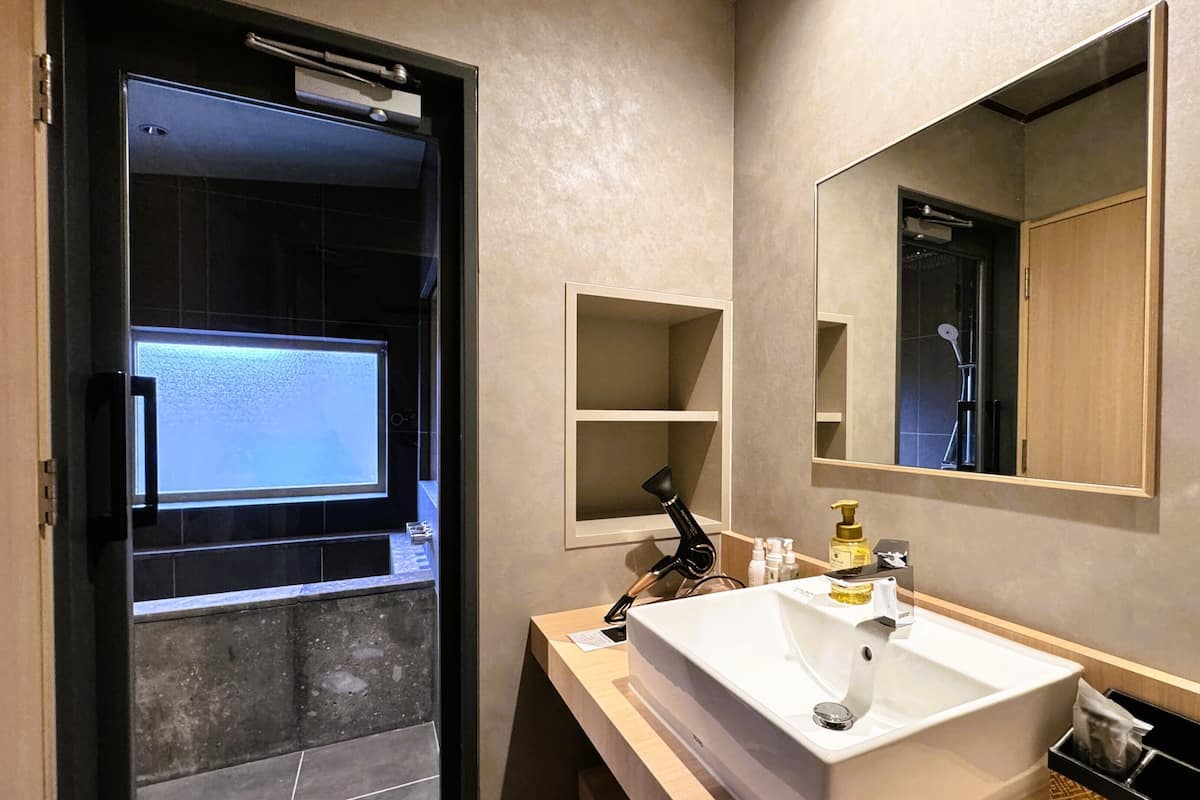 A bathroom with a large mirror, a sink, a shower, and a door leading to a shower area.