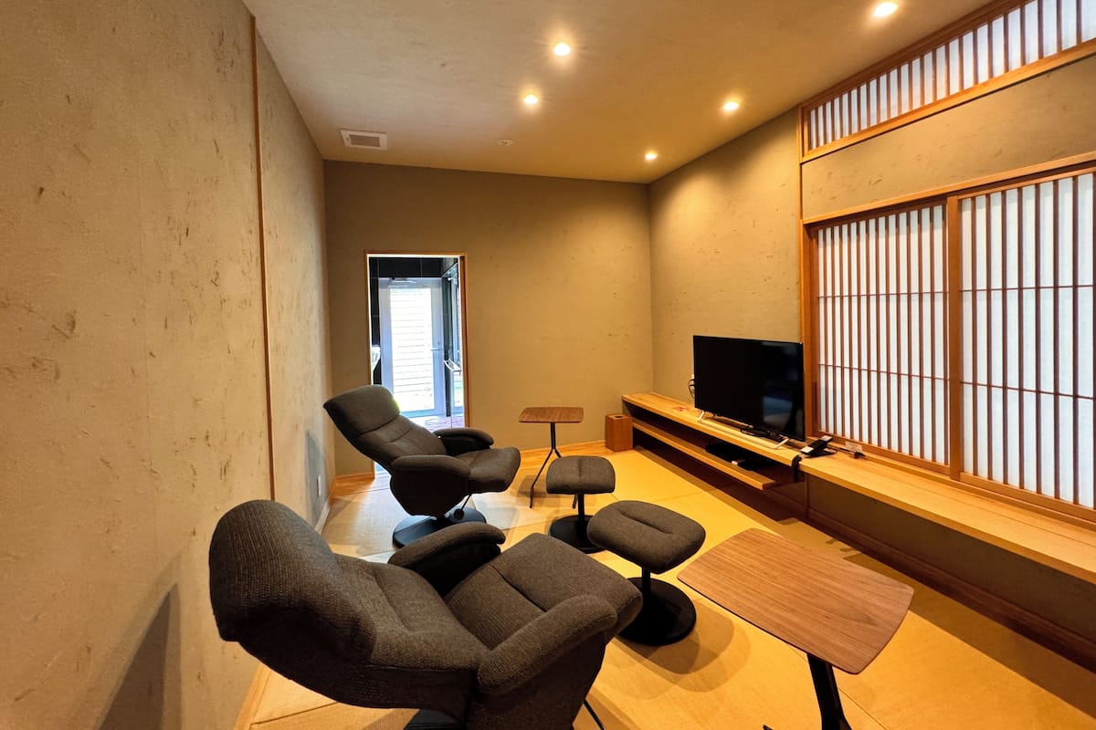 A modern living room with a flat-screen TV, two dark sofas, a small wooden table, and a sliding shoji screen.