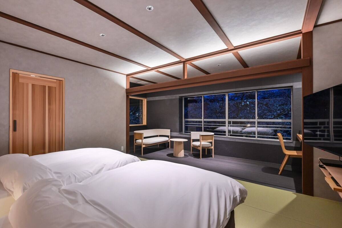 A modern hotel room with a bed, a desk, and a large window with a night view.