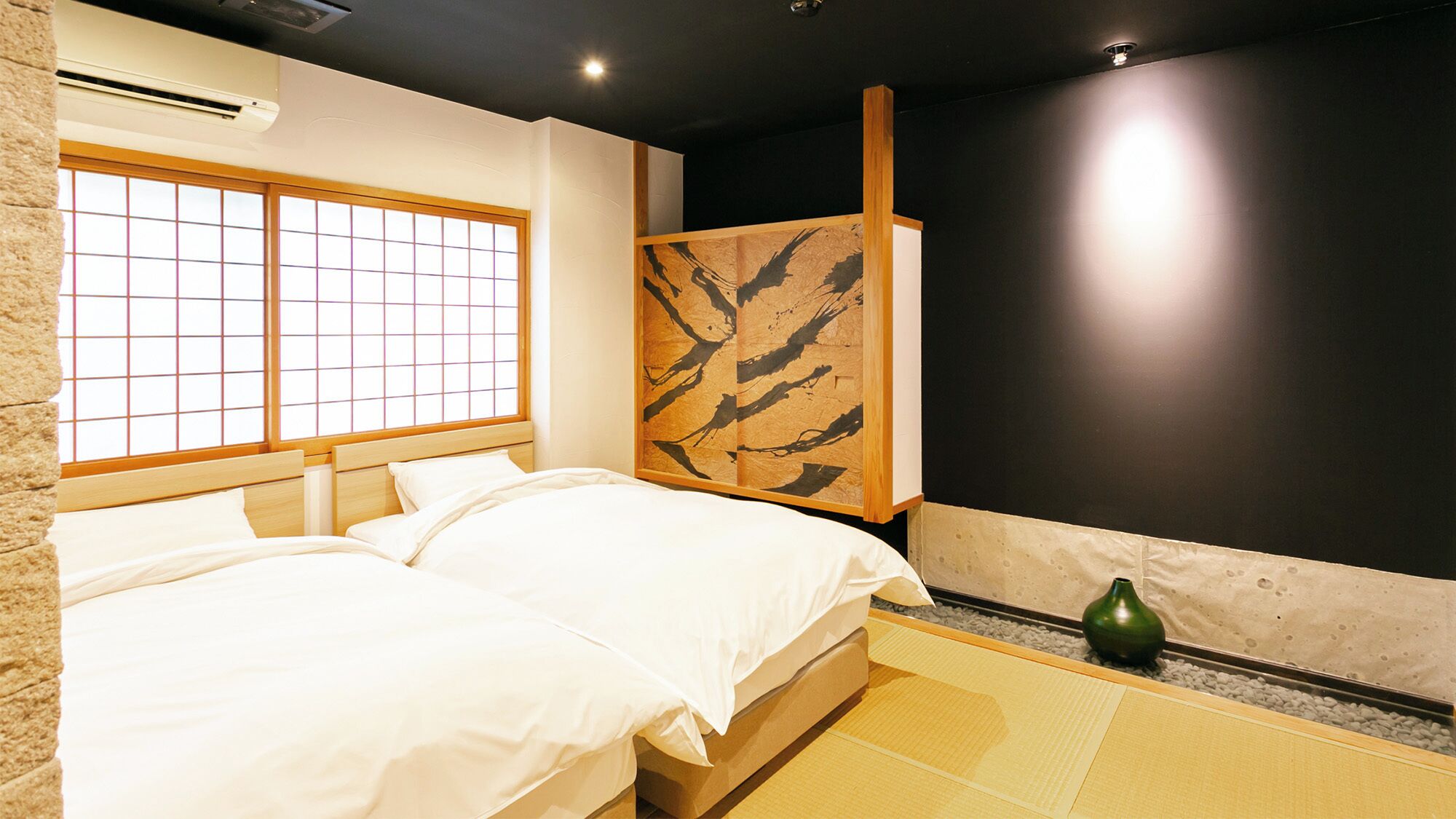 A room with a bed, a window with a grid pattern, a wooden panel with abstract design, and a dark wall.