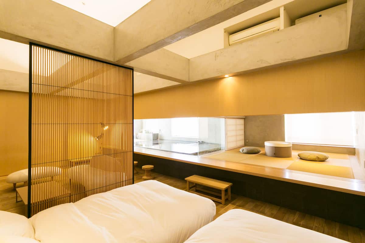 A modern hotel room with a large bed, a small seating area, a window with a view, and a sliding door.