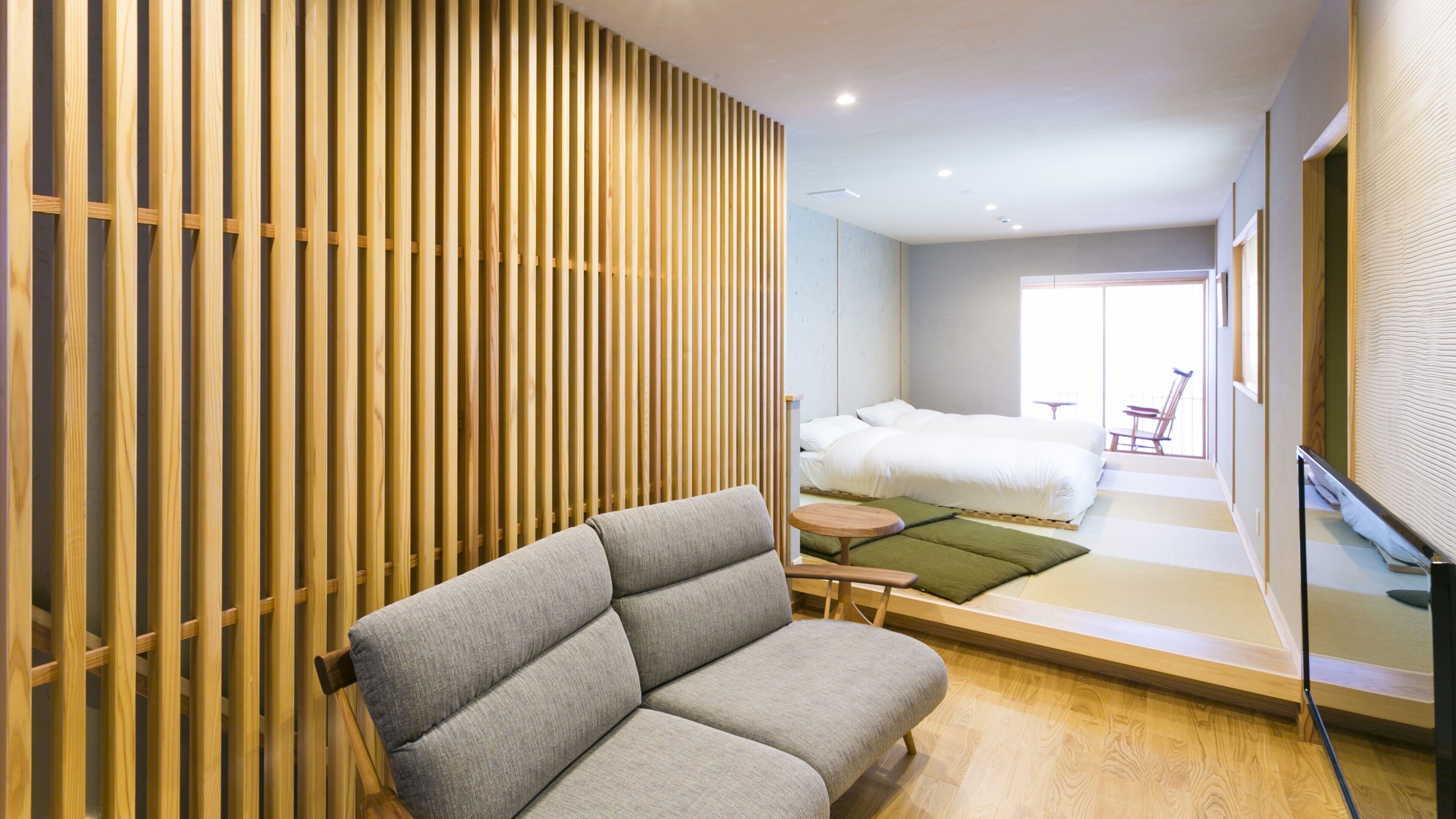 A modern hotel room with a sofa, a bed, a small table, and a view of the outside.