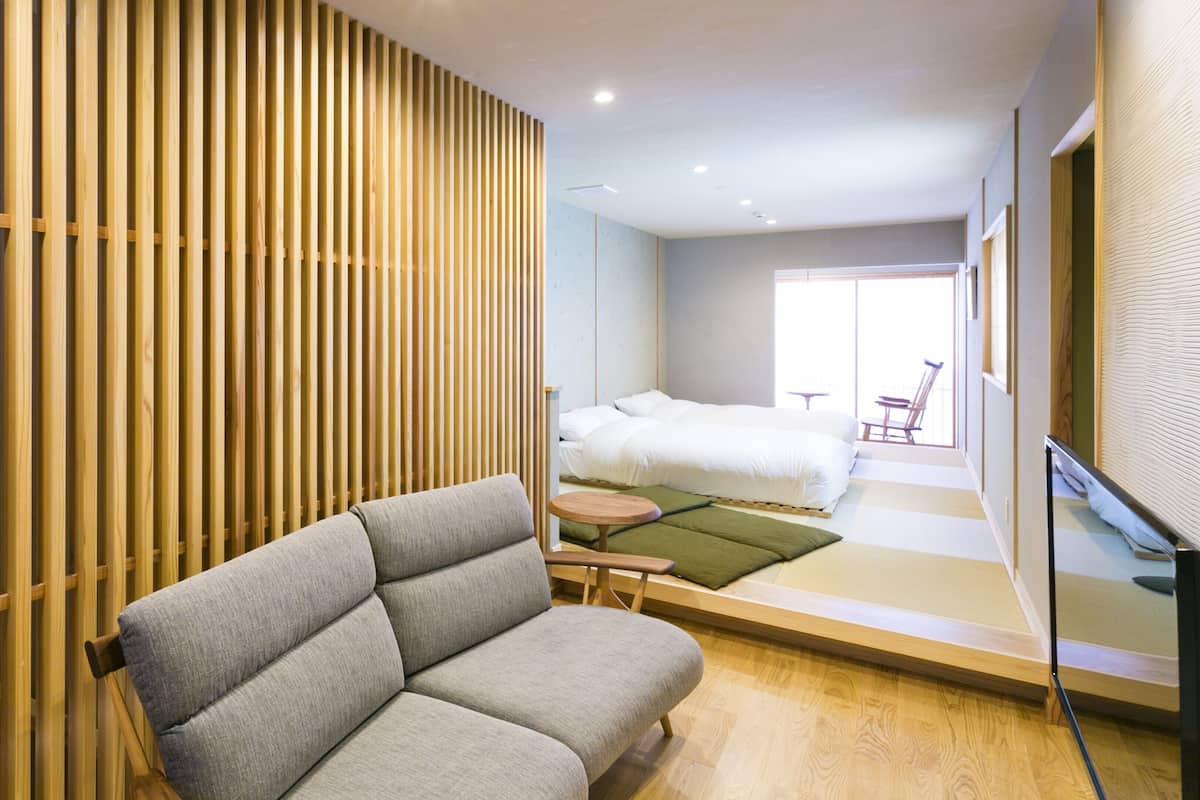 A modern hotel room with a sofa, a bed, a small table, and a view of the outside.