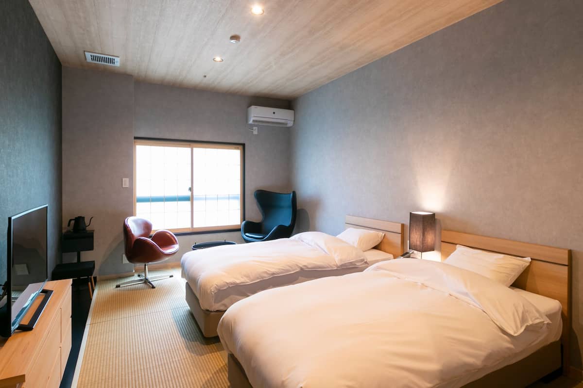 A hotel room with two beds, a TV, a desk, a chair, and a window with a view.
