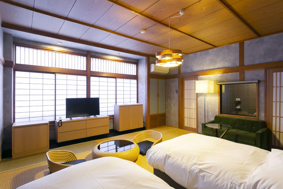 A hotel room with tatami flooring, a bed, a television, a green sofa, and a traditional Japanese-style window.