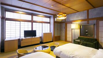 Une chambre d’hôtel avec un sol recouvert de tatamis, un lit, une télévision, un canapé vert et une fenêtre de style japonais traditionnel.
