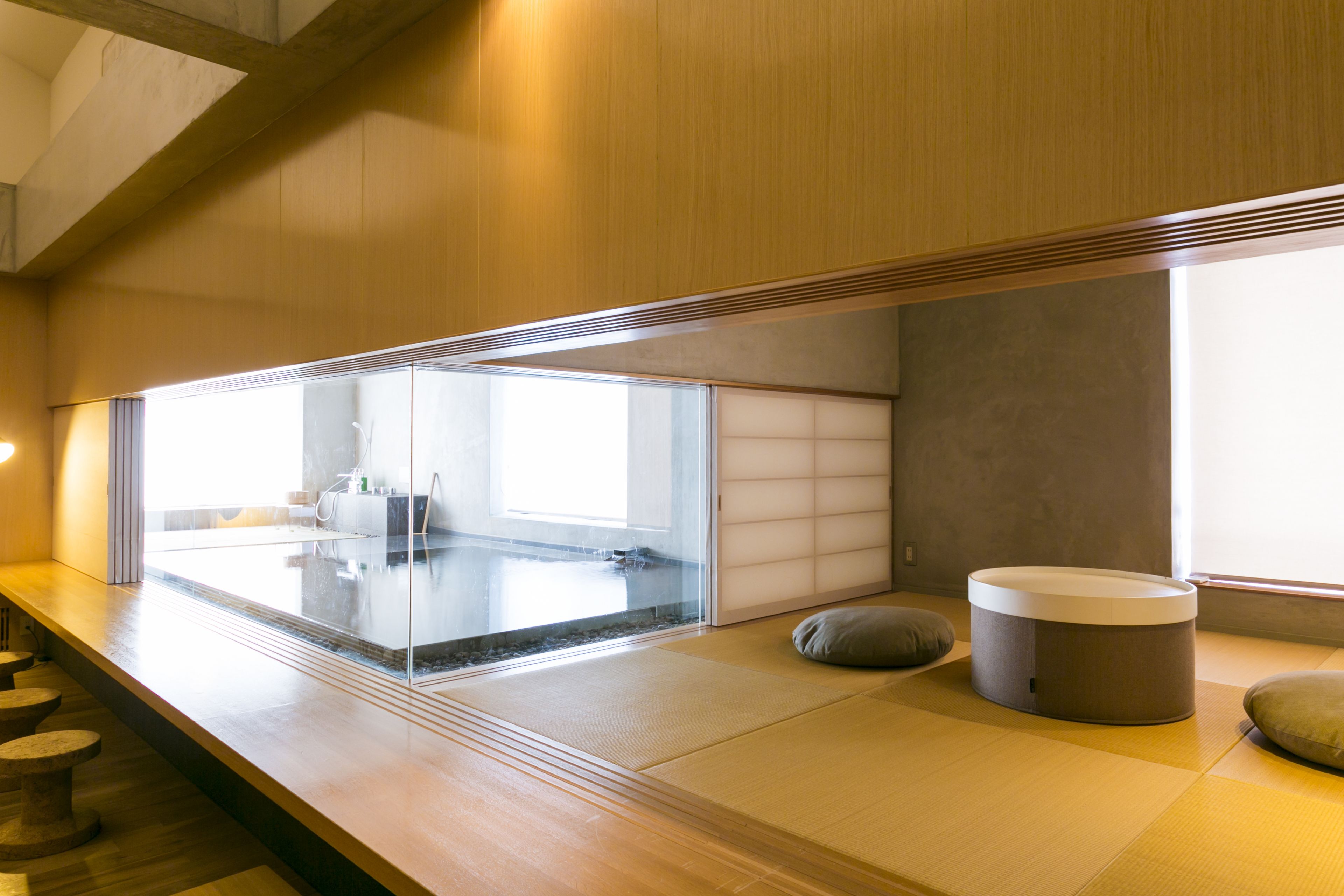 Un interior moderno con suelo de madera, una zona de estar con cojines y un panel de vidrio.