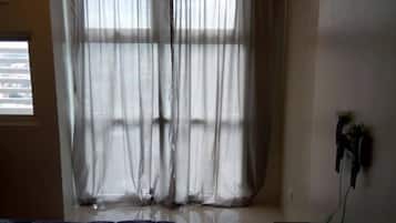 A bedroom with a bed, a window with sheer curtains, and a wall-mounted electrical outlet.