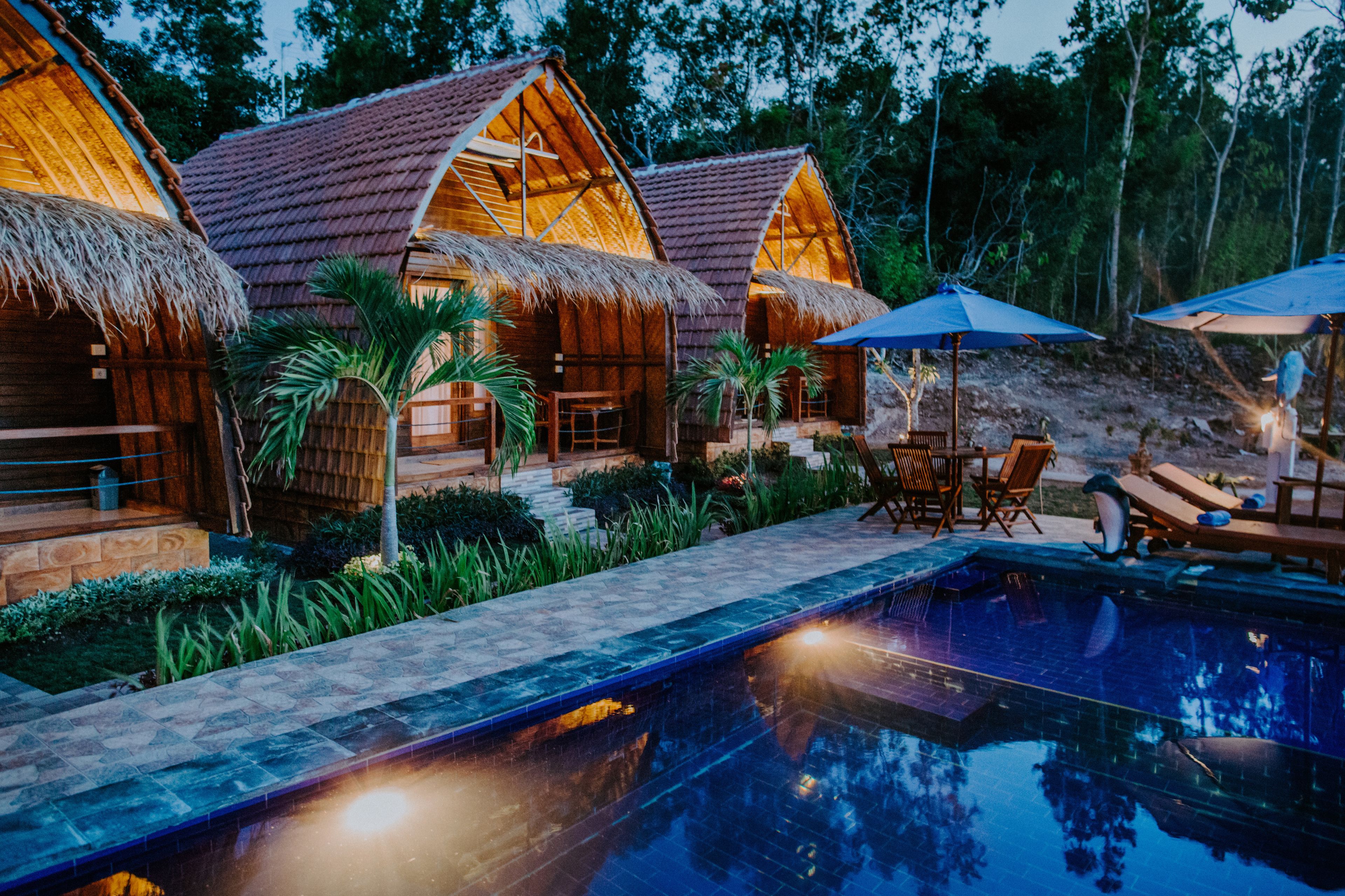 A poolside area with wooden cabins, lounge chairs, and a swimming pool.