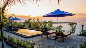 Zwembadgedeelte met ligbedden en parasols, met uitzicht op een wateroppervlak tijdens de zonsondergang.