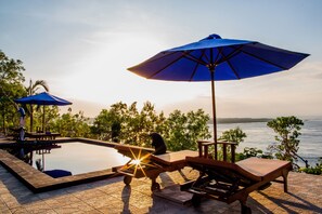 A poolside area with lounge chairs and umbrellas, overlooking a body of water. - Sundi Ocean Bungalow by ABM (Penida Island)