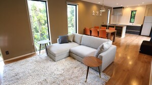 A modern living room with a sectional sofa, a round coffee table, and a dining area with orange chairs. - Tabinoteitaku Okinawa Bise Homann Concept (Motobu)