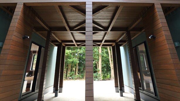 A covered walkway with wooden beams and columns, leading to a forested area. - Tabinoteitaku Okinawa Bise Homann Concept (Motobu)