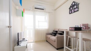 Una sala de estar moderna con un sofá, un televisor, una cafetera y una pequeña zona de bar con taburetes.