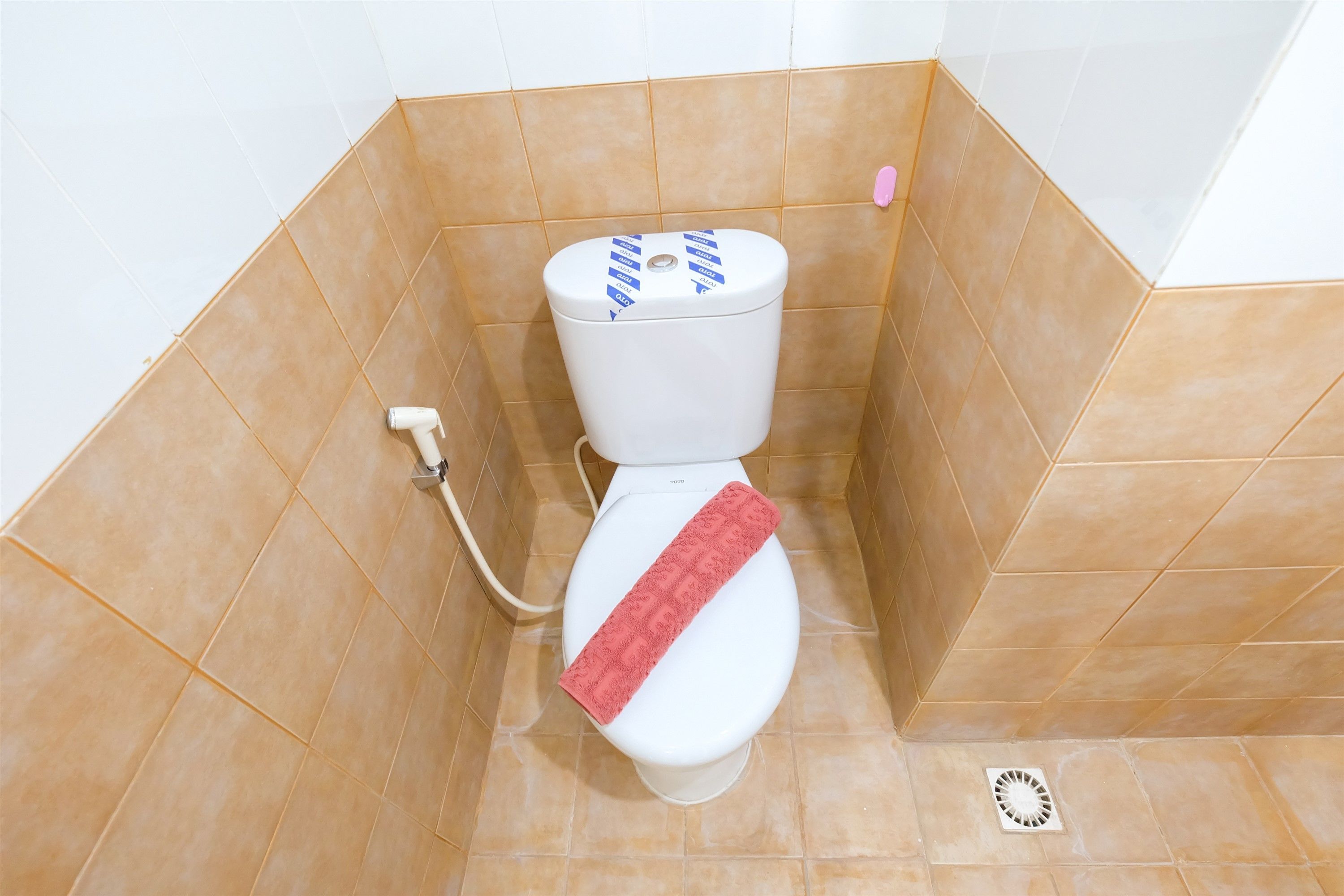 A toilet with a pink towel, a white toilet paper holder, and a pink soap dispenser in a bathroom with beige tiles.