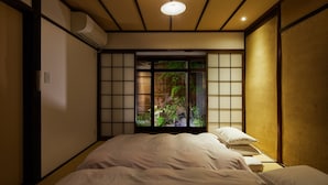 A traditional Japanese-style room with tatami flooring, a futon bed, a sliding shoji screen door, and a small bedside table with a pillow. - Tachibana an (Kyoto)