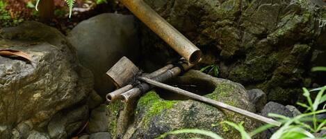 A rustic outdoor setting with a wooden structure, rocks, and greenery.