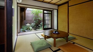 A traditional Japanese room with tatami flooring, a low table with a teapot, and a view of a garden through a sliding door. - Tachibana an (Kyoto)