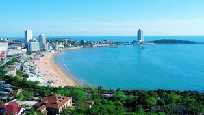 A coastal cityscape with a wide beach, high-rise buildings, and a clear view of the sea. - MG Hotel - St. Michael's Cathedral, Qingdao (Qingdao)