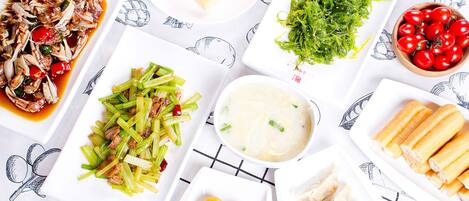 A variety of dishes including seafood, vegetables, and dumplings on a table with a patterned tablecloth.