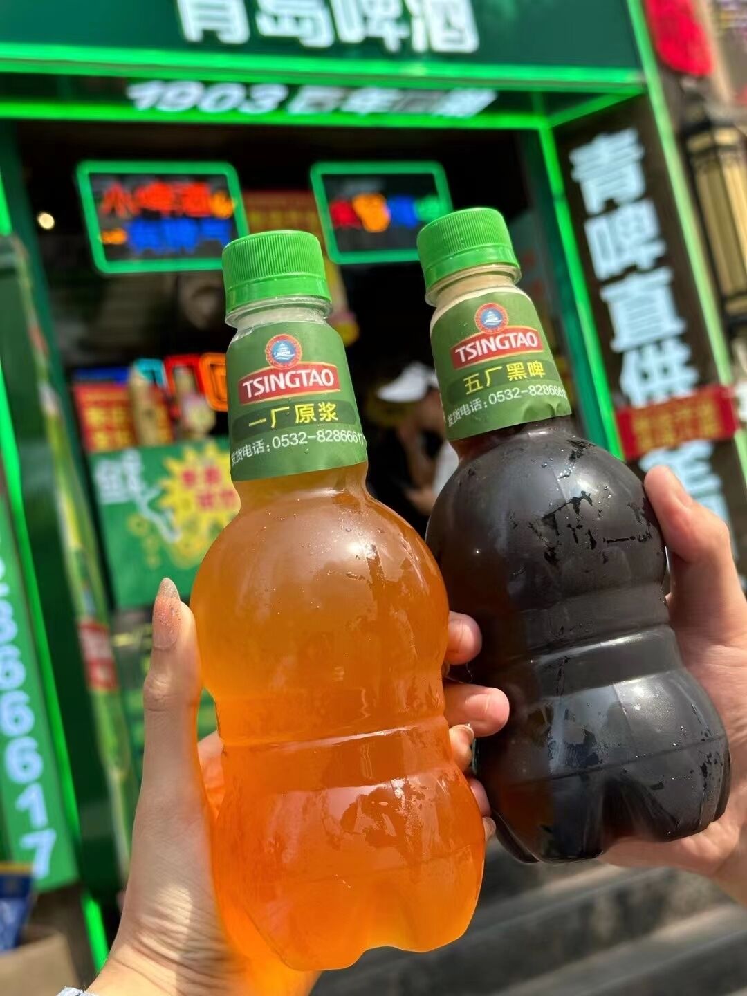 Two bottles of Tsingtao drink held by a person.
