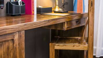 A wooden desk with a lamp, a red book, a black phone holder, and a trash bin.