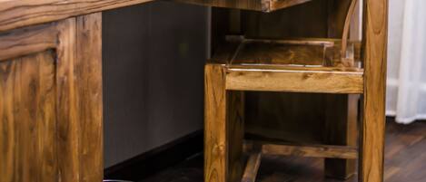 A wooden desk with a lamp, a red book, a black phone holder, and a trash bin.