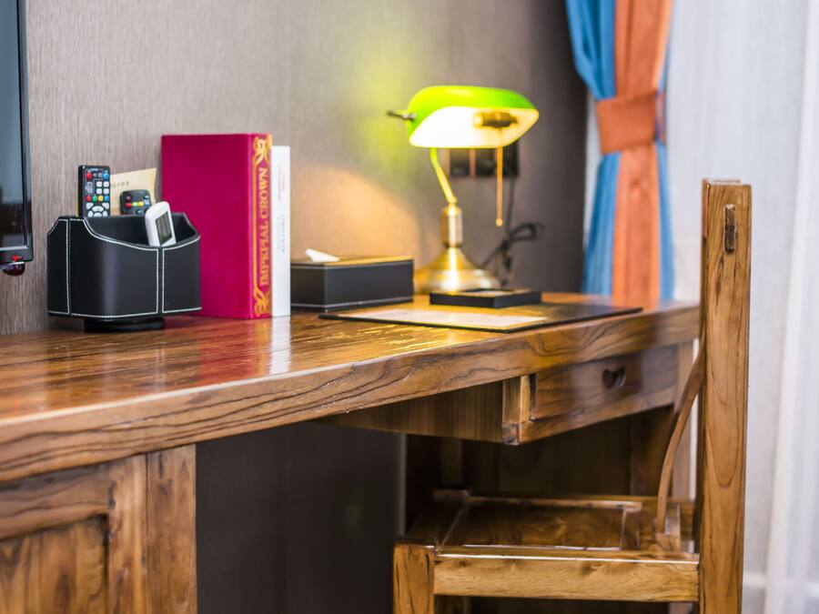A wooden desk with a lamp, a red book, a black phone holder, and a trash bin.